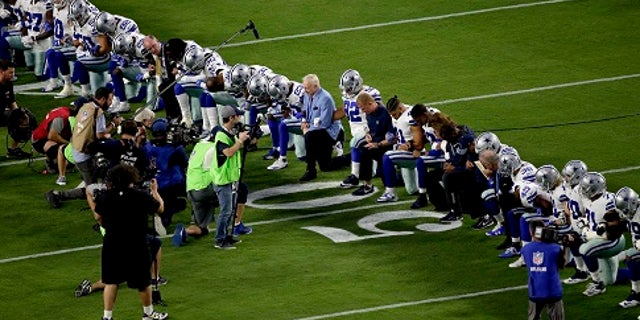 Dallas Cowboys owner Jerry Jones, center, takes a knee with the team prior to an NFL game against the Arizona Cardinals.