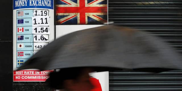 A pedestrian with an umbrella passes a board showing the exchange rates at a money exchange bureau in London, Monday, Jan. 16, 2017. The British pound fell to a three-month low amid reports Prime Minister Theresa May will signal her willingness to make a clean break with the European Union. Sterling fell below 1.20 US Dollars before recovering slightly Monday. (AP Photo/Kirsty Wigglesworth)
