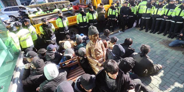 In this Dec. 28, 2016, photo, members of civic groups sit around a comfort-woman statue after they set up in front of the Japanese consulate as police officers surround them in Busan, South Korea. Japan is recalling its ambassador to South Korea Friday, Jan. 6, 2017 in response to the placing of the statue. Many Koreans and other women in Asia were forced to work in brothels for the Japanese military during World War II in what was called the "comfort-woman" system. (Kim Sun-ho/Yonhap via AP)