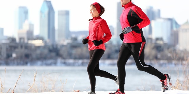 Runners running in winter snow with city skyline background. Healthy multiracial young couple. Asian woman runner and Caucasian man running with Montreal skyline, Quebec, Canada