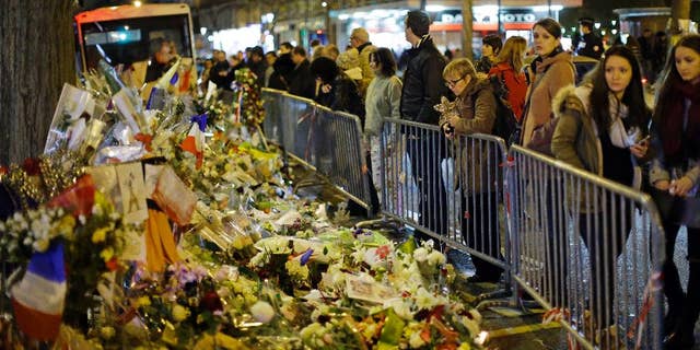People look at the floral tributes placed to honour the victims of the Paris attacks across from the Bataclan concert hall in Paris Saturday, Dec. 12, 2015. (AP Photo/Matt Dunham)