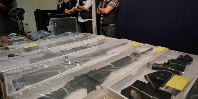 Plain clothed policemen stand guard in front of some air rifles and other evidences during a press conference in Hong Kong, Monday, June 15, 2015. Hong Kong police say they have arrested nine people, members of a local radical group and seized materials for making explosives. (AP Photo/Vincent Yu)