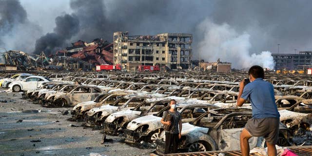 In this photo taken Thursday, Aug. 13, 2015, a man takes photo for another near charred remains of new cars at a parking lot near the site of a warehouse explosion in northeastern China's Tianjin municipality. People recently punished in China's campaign against online rumors include those who circulated an inflated death toll in the Tianjin blasts and who alleged a man committed suicide because of the country's stock market woes, state media reported Monday, Aug. 31, 2015.(AP Photo/Ng Han Guan)
