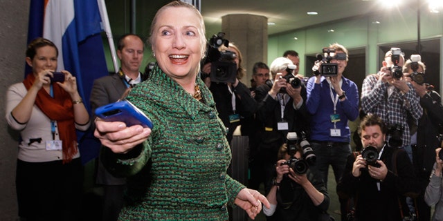 FILE - Dec. 8, 2011: Then-Secretary of State Hillary Rodham Clinton hands off her mobile phone after arriving to meet with Dutch Foreign Minister Uri Rosenthal at the Ministry of Foreign Affairs in The Hague, Netherlands.