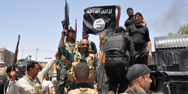 FILE --  Jun 28, 2014: Iraqi security forces hold up a flag of the the jihadist group ISIS that they captured during an operation to regain control of Dallah Abbas 35 miles outside of Baghdad, Iraq.