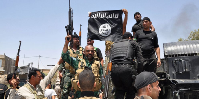FILE -- Jun 28, 2014: Iraqi security forces hold up a flag of the the jihadist group ISIS that they captured during an operation to regain control of Dallah Abbas 35 miles outside of Baghdad, Iraq.