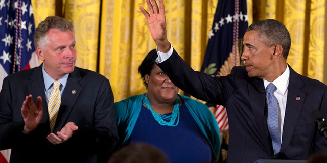 July 21, 2014: Virginia Governor Terry McAuliffe, left, applauds as President Obama waves after signing an executive order to protect LGBT employees from federal workplace discrimination in the East Room of the White House in Washington. Obama's executive order prohibits discrimination against gay and transgender workers in the federal government and its contracting agencies, without a new exemption that was requested by some religious organizations.