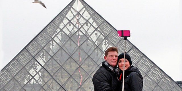 FILE -- Jan. 6, 2015: Chris Baker and Jennifer Hinson from Nashville, Tennessee, use a selfie stick in front of the Louvre Pyramide in Paris.