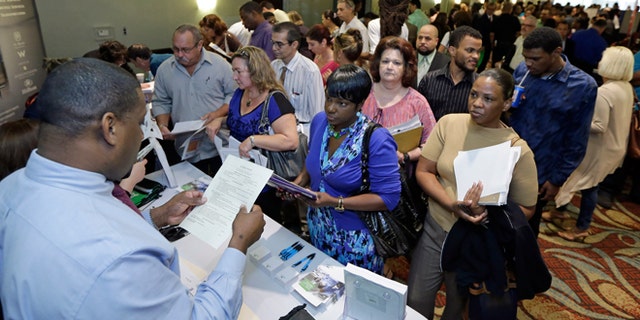 FILE -- Oct. 22, 2014: Russell Neal, left, gives job information to job seeker Queena Moise, foreground second from right, at a job fair in Miami Lakes, Fla.