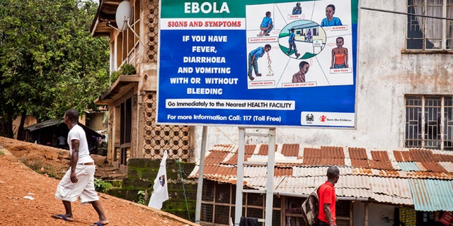 People walk past a billboard encouraging people suffering from symptoms linked to Ebola to present themselves at a health facility for treatment in Freetown, Sierra Leone, Thursday,  Aug. 7, 2014. (AP Photo/ Michael Duff)