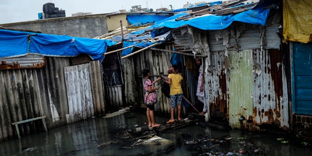 Residents stand in a flooded street outside their house at a slum in Mumbai July 16, 2014. Weak rainfall in India since the start June, when the monsoon season began, has raised concerns of a first drought in five years, although weather experts are hopeful rains will revive in the next week. REUTERS/Danish Siddiqui (INDIA - Tags: SOCIETY ENVIRONMENT POVERTY) - RTR3YWFK