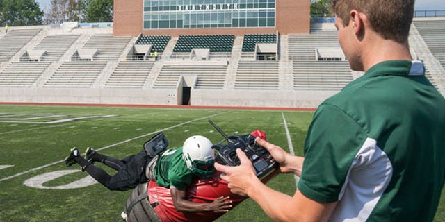 Victor Williams ’16 tackles the Mobile Virtual Player, which he and his teammates will use at practice. Quinn Connell ’13, Thayer ’14, controls the device, which he and other Thayer engineers helped develop.