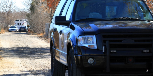 A Bernalillo County sheriff's deputy blocks the dirt road that leads to a home where detectives on Sunday, Jan. 20, 2013, were investigating the deaths of five people who were shot to death south of Albuquerque, N.M.