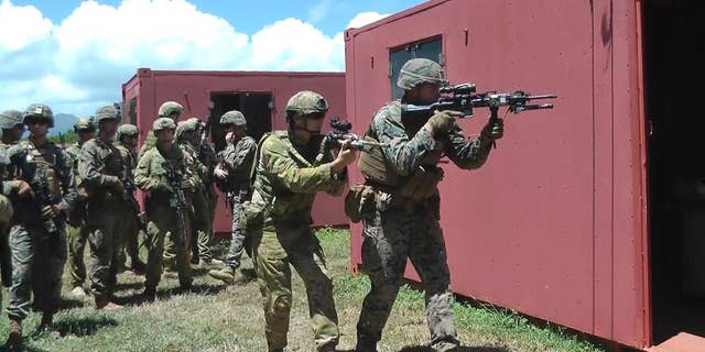 In this Thursday, July 7, 2016 photo, an Australian soldier, center left, and a U.S. Marine, right, get ready to raid a building at a mock urban combat training center in Kaneohe Bay, Hawaii. Australian soldiers are expected to lead a battalion of troops in the storming of a Hawaii beach during the world's largest maritime exercises this month, displaying the amphibious military skills they've been building up in recent years. (AP Photo/Audrey McAvoy)