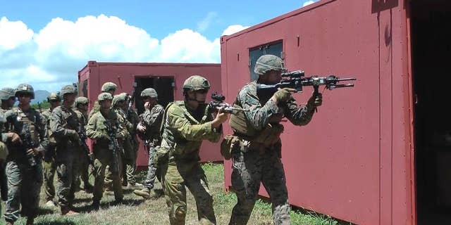 In this Thursday, July 7, 2016 photo, an Australian soldier, center left, and a U.S. Marine, right, get ready to raid a building at a mock urban combat training center in Kaneohe Bay, Hawaii. Australian soldiers are expected to lead a battalion of troops in the storming of a Hawaii beach during the world's largest maritime exercises this month, displaying the amphibious military skills they've been building up in recent years. (AP Photo/Audrey McAvoy)