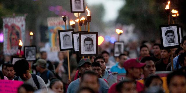 FILE - In this Dec. 26, 2015 file photo, relatives of the 43 missing students from the rural teachers college march holding pictures of their missing loved ones during a protest in Mexico City. Argentine forensic experts who have studied a dump in southern Mexico where government officials claim the bodies of 43 missing teachers’ college students were burned say a new investigation of the site is incomplete and inconclusive. The Argentine Forensic Anthropology Team was called in shortly after the students from the Rural Normal School at Ayotzinapa disappeared in Iguala in Guerrero state on Sept. 26, 2014. (AP Photo/Marco Ugarte, File)