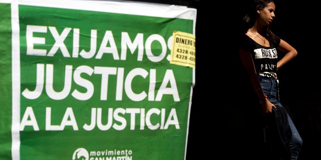 A woman stands next to a poster that reads in Spanish "Demand justice to justice", in reference to march organized by federal prosecutors demanding justice after the death of special prosecutor Alberto Nisman almost a month ago, in Buenos Aires, Argentina, Friday, Feb. 13, 2015. Nisman accused President Cristina Fernandez, Foreign Minister Hector Timerman and others in her administration of brokering the cover-up in the bombing of a Jewish community center in exchange for favorable deals on oil and other goods from Iran. Fernandez and Timerman have strongly denied the accusations, and Iran has repeatedly denied involvement in the bombing, which killed 85 people. (AP Photo/Rodrigo Abd)