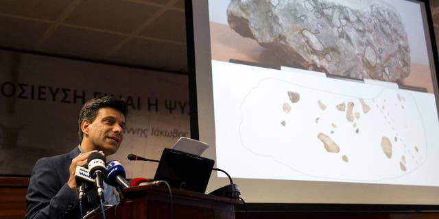 Greek archaeologist Christofilis Maggidis speaks as a photograph of a stone he believes belonged to the lost royal throne in the ancient palace of Mycenae, heart of the Mycenaean civilization, in southern Greece, during a press conference in Athens, on Tuesday, June 14, 2016. Maggidis says the worked stone, found by chance two years ago under the prehistoric citadel, is a chunk of the monolithic throne that was smashed when an earthquake sent part of the palace tumbling into a streambed below. (AP Photo/Petros Giannakouris