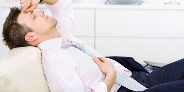 Mid-adult businessman lying on sofa at office, looking tired, eyes closed. Bright background.