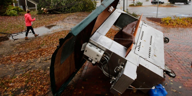 A woman walks by a food stand and a tree that were toppled by a storm in Freeport, Maine.