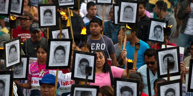 FILE - In this April 26, 2016 file photo, family members and supporters of 43 missing teachers college students carry pictures of the students as they march to demand the case not be closed and that experts' recommendations about new leads be followed, in Mexico City. The most recent forensic investigation of the southern Mexico garbage dump where the government says 43 students were incinerated did not confirm there was a fire there that night. It shows the experts found evidence the Cocula dump had been the site of at least five fires, but could not determine when. Remains of 17 people were also found, but it was unknown when they were burned. (AP Photo/Rebecca Blackwell, File)