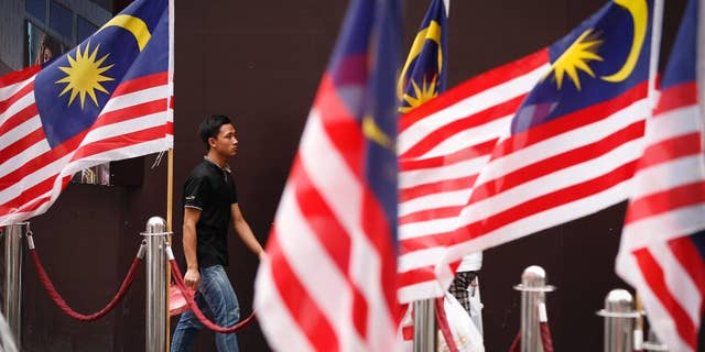 A man walks by displays of Malaysian national flags outside a shopping mall in Kuala Lumpur, Malaysia Wednesday, Aug. 12, 2015. A Malaysian opposition party Wednesday filed a civil lawsuit against Prime Minister Najib Razak for alleged election offenses involving $700 million in his bank accounts. (AP Photo/Vincent Thian)