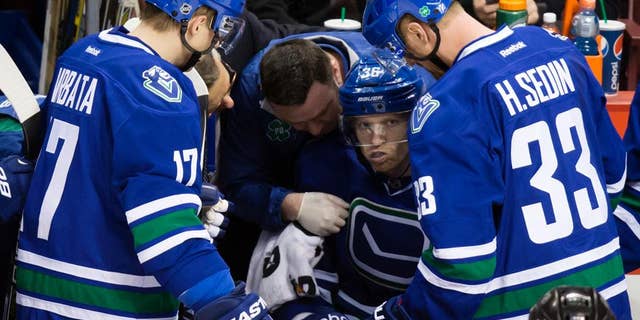 Vancouver Canucks' Jannik Hansen, center, of Denmark, is tended to by a trainer as Radim Vrbata, of the Czech Republic, and Henrik Sedin, right, of Sweden, watch after he was checked during the second period of an NHL hockey game against the Calgary Flames in Vancouver, British Columbia, on Saturday, Dec. 20, 2014. (AP Photo/The Canadian Press, Darryl Dyck)