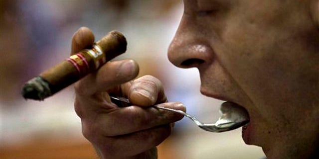 A man eats a dessert as he smokes a cigar during a tobacco cooking event at the 15th Cigar Festival in Havana, Cuba.