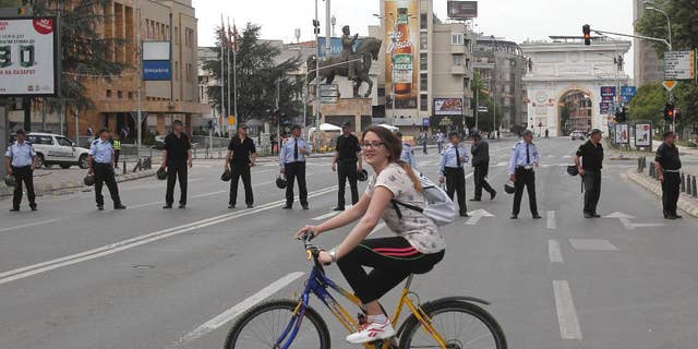 A girl rides a bicycle near a police cordon that blocks the street in front of the parliament building in Skopje, Macedonia, Friday, April 28, 2017. More than 100 people were injured Thursday evening including protestors, policemen and lawmakers, after protesters broke through a police cordon and entered Macedonian parliament to protest the election of a new speaker, despite a months-long deadlock in talks to form a new government. (AP Photo/Boris Grdanoski)