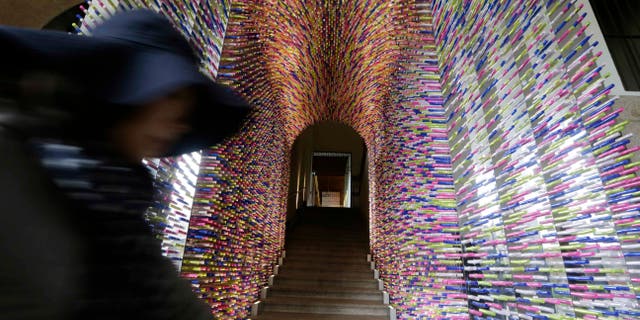 A woman passes by an installation called "Transition", made with lipstick packages, part of the Milan's Furniture Fair, in Milan, Italy, Monday, April 8, 2012. The 52nd International Furniture Fair (Salone del Mobile) opens in Milan on Tuesday, April 9, 2013 until April 14. (AP Photo/Luca Bruno)