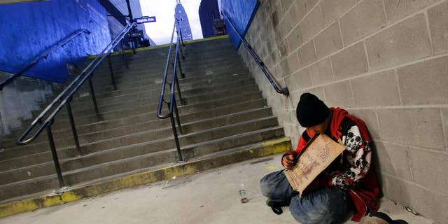FILE - In this Oct. 9, 2015 file photo, a homeless man holds a sign asking for money while sitting at the entrance to a subway station in New York. New York City plans to deploy hundreds of outreach workers who will canvass much of Manhattan every day with a deceptively simple goal: talk to as many homeless people as possible, as often as possible. Through frequent contact, the city hopes to persuade the chronic homeless, even those living on the street for years, to go to shelters. (AP Photo/Mark Lennihan, File)