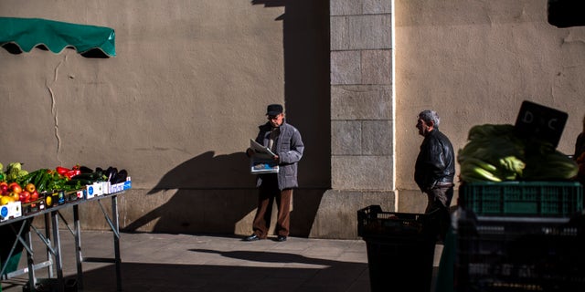 A man reads a newspaper at a fruit market in Barcelona, Spain, Tuesday Jan. 22, 2013. Spain has sold euro 2.8 billion ($3.7 billion) in short-term bills and seen the interest rates it has to pay fall sharply. Spain's borrowing costs have dropped from unsustainable highs last year after the European Central Bank offered to help countries struggling with their debts if they apply for aid. (AP Photo/Emilio Morenatti)