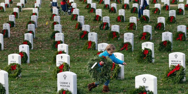 A child carries a wreath to a grave during Wreaths Across America at Arlington National Cemetery, Saturday, Dec. 12, 2015, in Arlington.
