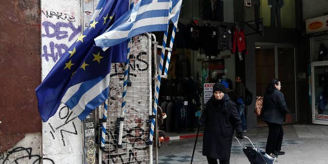 A woman pulls a shopping trolley next to a Greek and an EU flags at a main street of Athens, Thursday, Jan. 26, 2017. Greece's prime minister on Wednesday marked two years in office, as talks with bailout lenders remain at an impasse. (AP Photo/Yorgos Karahalis)
