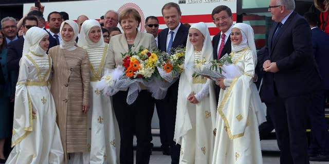 German Chancellor Angela Merkel, center-left, EU Council President Donald Tusk, center-right, Turkish Prime Minister Ahmet Davutoglu, second right, and EU Commission Vice President Frans Timmermans, right, are greeted by Syrian refugee children at a Syrian refugee camp in Nizip, Gaziantep, Turkey, Saturday, April 23, 2016. Merkel and top European Union officials, under pressure to reassess a migrant deportation deal with Turkey, were traveling close to Turkey's border with Syria on Saturday in a bid to bolster the troubled agreement. Davutoglu's wife Sare Davutoglu is at the left. (Hakan Goktepe/Pool Photo via AP)