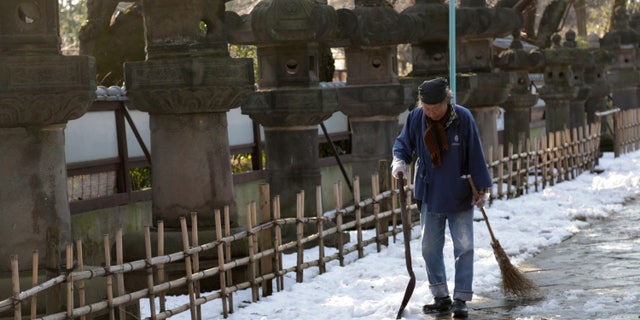 A worker walks away after shoveling snow off a court yard at a temple in Tokyo, Sunday, Feb. 16, 2014. (AP Photo/Shizuo Kambayashi)