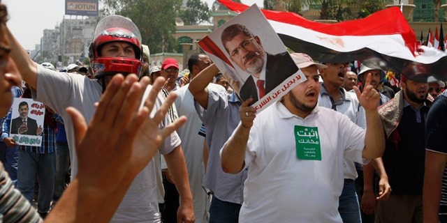 Supporters of Egypt's ousted President Mohammed Morsi wave Egyptian flags and his picture at a sit-in in Nasser City, suburb of Cairo, Egypt, Sunday, July 7, 2013. Egypt's new president moved to assert his authority and regain control of the streets Saturday even as his Islamist opponents declared his powers illegitimate and issued blood oaths to reinstate Mohammed Morsi, whose ouster by the military has led to dueling protests and deadly street battles between rival sides. (AP Photo/Paul Schemm)