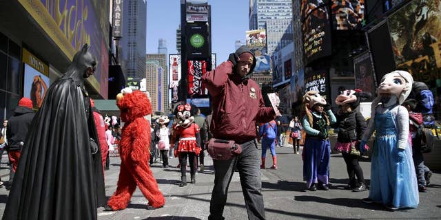 FILE - In this March 29, 2016 file photo, a bus tour ticket seller, center, walks through a group of costumed characters in Times Square in New York. New York City workers have started painting teal rectangles in pedestrian plazas designating where costumed characters can pose with tourists in Times Square. Starting June 21, street performers and costumed characters will be restricted to those areas when soliciting tips from tourists. (AP Photo/Seth Wenig)
