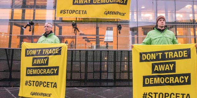 Greenpeace demonstrators hold protest banner outside a meeting venue of EU trade ministers at the EU Council building in Luxembourg, Tuesday, Oct. 18, 2016. European Union trade ministers meet Tuesday to discuss the Comprehensive Economic and Trade Agreement between the EU and Canada. (AP Photo/Olivier Matthys)
