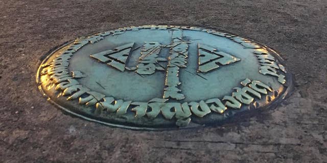 FILE - In this Oct. 2, 2016, file photo, a small bronze plaque commemorating Thailand's 1932 revolution rests in the pavement of the Royal Plaza in Bangkok, Thailand. In early April, the plaque was mysteriously removed by parties unknown and substituted by one praising the Chakri Dynasty, whose 10th king took the throne last December. The Foreign Correspondents' Club of Thailand has accepted a police request that it cancel a panel discussion on the mysterious theft of a plaque commemorating the end the country's absolute monarchy in 1932. (AP Photo/Apichart Khunnawatbandit)