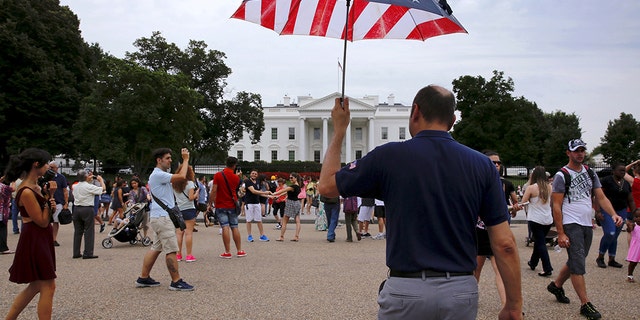 Tour guide David Machado uses a U.S. flag-themed umbrella to stay visible to his tour group as they visit the White House in Washington, August 2015