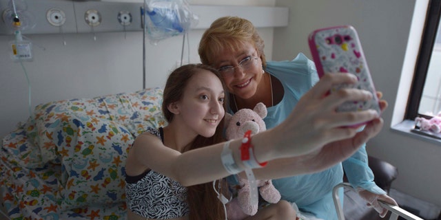 FILE - In this Feb 28, 2015 file photo released by Chile's Presidential Press Office, Valentina Maureira takes a photo of herself with President Michelle Bachelet, at the Catholic University hospital in Santiago, Chile. The girl, ailing from cystic fibrosis, who made a public plea for permission to end her life has died. Her father, Fredy Maureira, confirmed that Valentina passed away on Thursday, May 13, 2015, to local Radio Bio Bio, saying the 14-year-old is finally resting in peace. (AP Photo/Chile Presidential Press Office, Ximena Navarro, File)