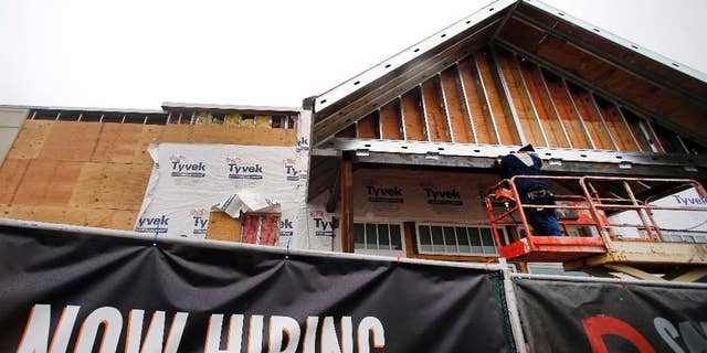 FILE - In this Jan. 12, 2015 file photo, a now hiring sign hangs nearby as a builder works on a commercial property under construction in Peabody, Mass. The Labor Department reports on state unemployment rates for December on Tuesday, Jan. 27, 2015. (AP Photo/Elise Amendola, File)