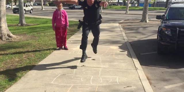 In this Wednesday, March 30, 2016 still frame from video provided by the Huntington Beach, Calif., Police Department, Officer Zach Pricer shows an 11-year-old homeless girl how to hopscotch on a street in Huntington Beach, Calif. Officers found the girl and her mother living in a car in a parking lot Wednesday. While other officers reached out to the department's homeless task force, Pricer turned to hopscotch to make the girl feel more comfortable, knowing a police officer can seem scary to a child. (Huntington Beach Police Department via AP)