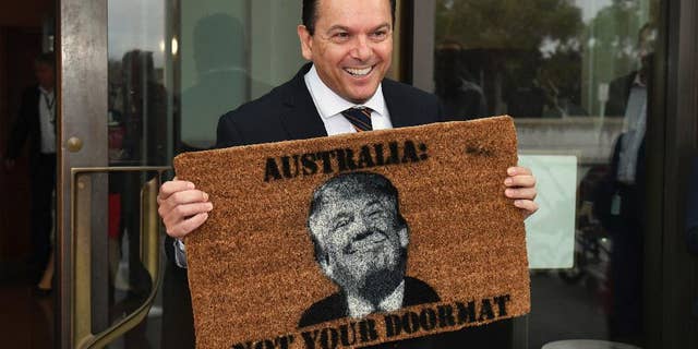 Australian Senator Nick Xenophon arrives at the Senate entrance at Parliament House in Canberra, holding a doormat featuring an image of United States President Donald Trump, Tuesday, Feb. 7, 2017. (Mick Tsikas/AAP Image via AP)