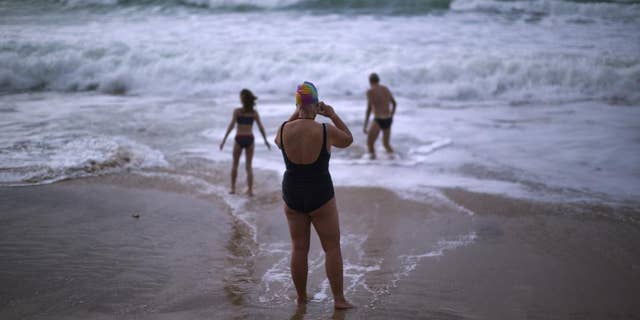 FILE- In this Jan. 1, 2014 file photo, German tourists walk on the seashore as one of them takes a photograph, after swimming in the Atlantic ocean in a beach in Cadiz, southwest Spain. Nudists have lost a seven-year legal battle for access to a popular tourist resort beach on Spain's southwestern tip. (AP Photo/Emilio Morenatti, File)