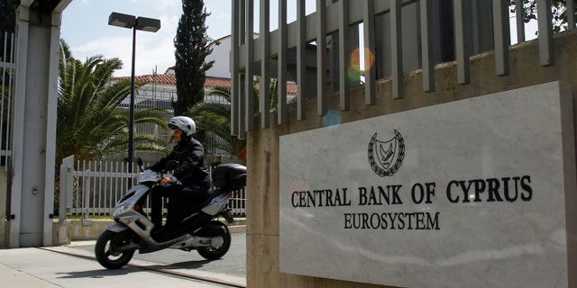 FILE - The March 13, 2012 file photo shows a man on a scooter, exiting from a gate of Central Bank of Cyprus in Nicosia, Cyprus. When it came to helping out Greece, Ireland and Portugal, Germany grudgingly went along with its European partners and backed hundreds of billions in rescue loans. But now that tiny Cyprus is in trouble, German politicians for the first time appear in no mood to help _ which could put the Mediterranean island country on the path to bankruptcy and out of the eurozone. (AP Photo/Petros Karadjias)