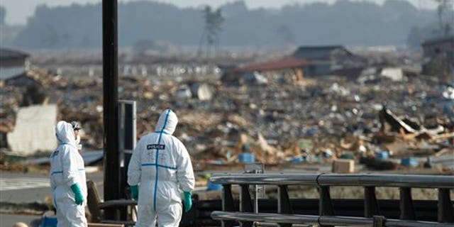 April 15: Japanese police officers stand by bodies of victims while searching for missing people at a devastated area in Namie of Fukushima Prefecture, northeastern Japan. In the background is part of the Fukushima Dai-ichi nuclear complex. (AP)