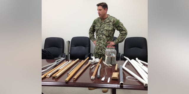 In this image reviewed by the U.S. Military, Navy Capt. Robert Durand stands next to some of the makeshift weapons, including broomsticks and batons made of plastic and steel, that were confiscated from prisoners at the Guantanamo Bay prison following a Saturday clash between prisoners and guards, on display for the press at the U.S. Naval Base Guantanamo Bay in Cuba, Tuesday, April 16, 2013. Soldiers with riot helmets and shields swept into recreation yards and met with resistance from several dozen prisoners, the leadership of the detention center said. The guard force raided Camp 6 because the prisoners had for several weeks covered up 147 of the 160 security cameras, making it impossible to monitor them amid a weeks long hunger strike. The hunger strike goes on, with 45 prisoners refusing meals and 13 being force fed, officials said. (AP Photo/Ben Fox)