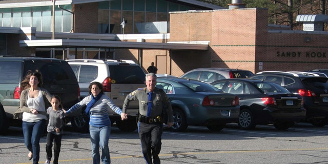 Dec. 14, 2012: In this file photo provided by the Newtown Bee, a police officer leads two women and a child from Sandy Hook Elementary School.